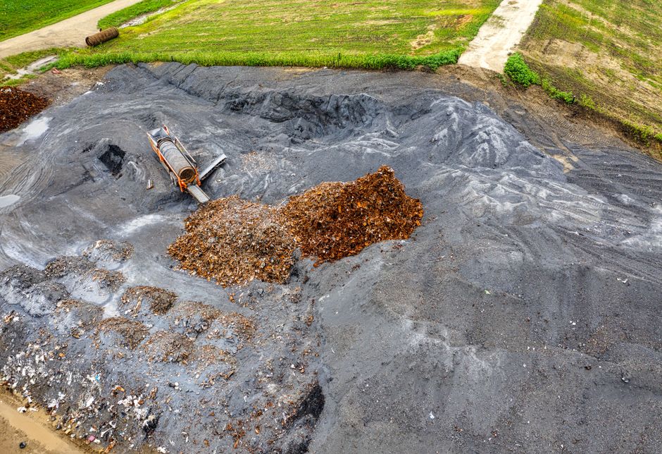 Aerial photograph showcasing a pile of waste material on black soil in an open field.